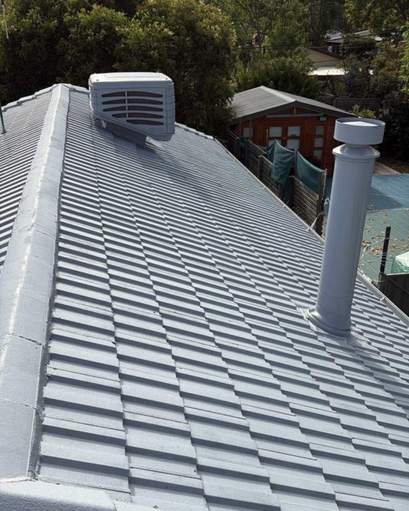 Concrete tile roof coated in light grey, with coated ridge capping, a vent and a flue