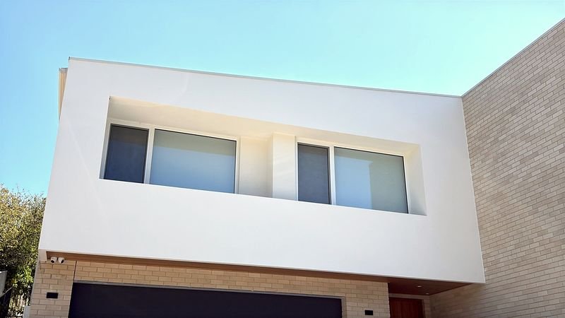 Two-storey new build with a white rendered upper storey over face brick, seen from below